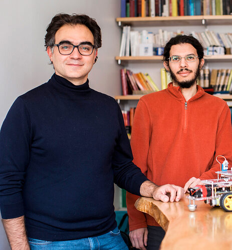 Photo of Vincenzo Vitelli in a black turtleneck and Michel Fruchart in an orange shirt in front of their wheeled robots